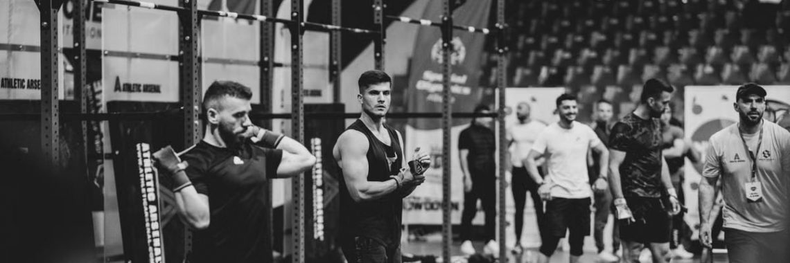 Black and white image of a fitness competition showcasing athletes and weights in a gym setting.
