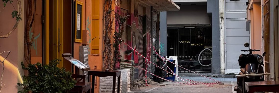 Explore a quaint alleyway in Athens, Greece, featuring inviting cafés and warm colors on a sunny day.